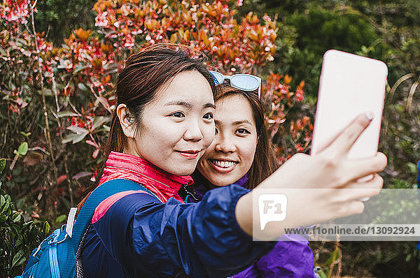 Female friends taking selfie with mobile phone while standing by trees