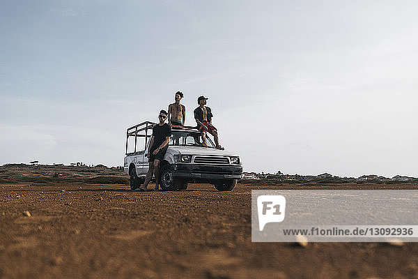 Friends relaxing on pick-up truck against sky