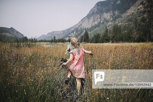 Rückansicht eines unbekümmerten Mädchens  das im Yellowstone-Nationalpark inmitten eines Grasfeldes gegen die Berge läuft