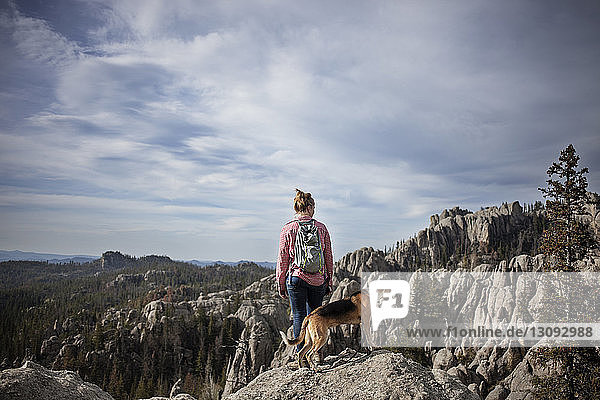 Frau und Hund stehen auf Felsen gegen Berge und Himmel