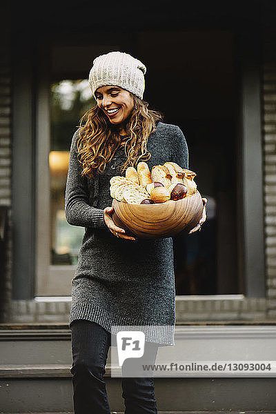 Happy woman carrying various breads in wooden bowl