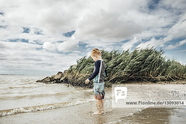 Side view of boy standing at beach against cloudy sky