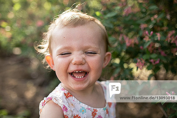 Close-up of happy baby girl standing against plants at park