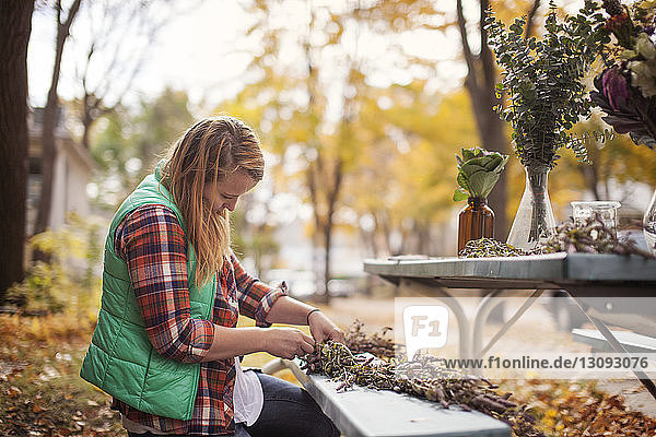 Side view of woman making flower decoration on bench at field