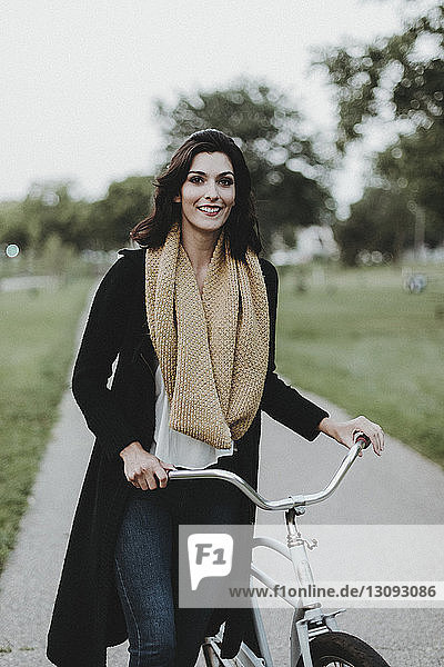 Portrait of smiling woman with bicycle at park