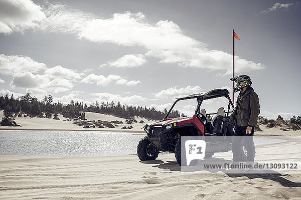 Mann mit Golfwagen auf Sand am Teich stehend