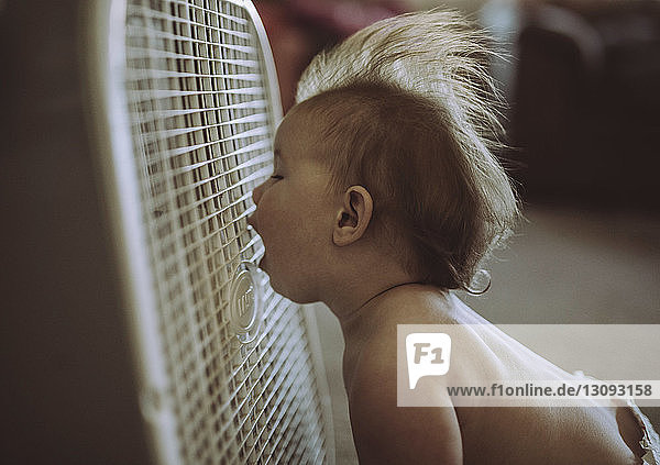 Kleiner Junge ohne Hemd mit offenem Mund  der zu Hause eine Brise aus der Klimaanlage genießt
