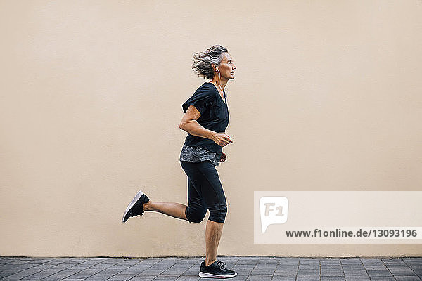 Side view of woman jogging on footpath against wall