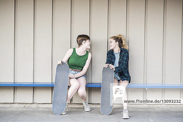 Teenager-Freunde mit Skateboards unterhalten sich  während sie auf einer Bank an der Wand sitzen