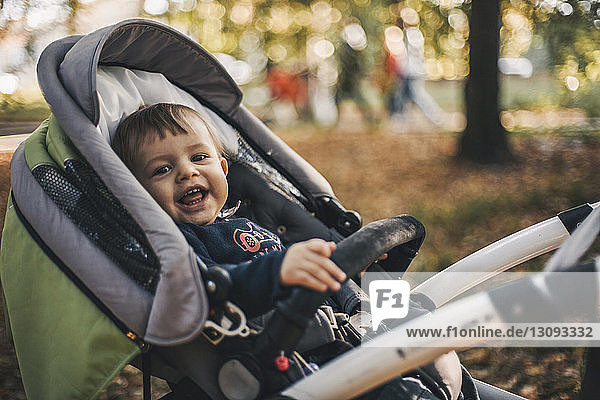 Porträt eines fröhlichen Kleinkindes  das im Herbst auf einem Kinderwagen im Park liegt