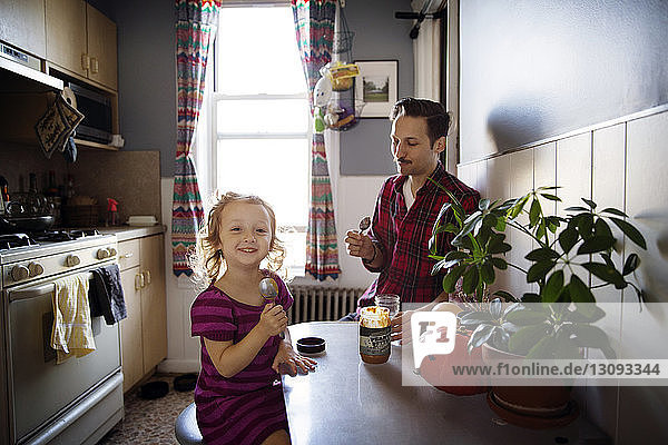 Mädchen und Vater essen Erdnussbutter  während sie in der Küche am Tisch sitzen