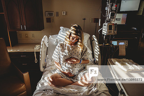 Schwangere Frau berührt Bauch  während sie im Krankenhaus auf dem Bett sitzt