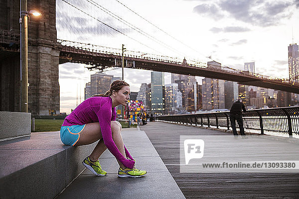 Frau schnürt Schuhschnürsenkel  während sie auf Stufen vor der Brooklyn-Brücke sitzt