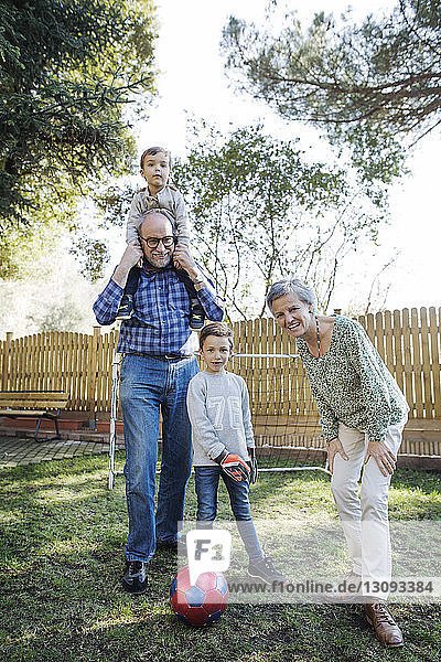 Portrait of happy grandparents with grandsons playing soccer at yard