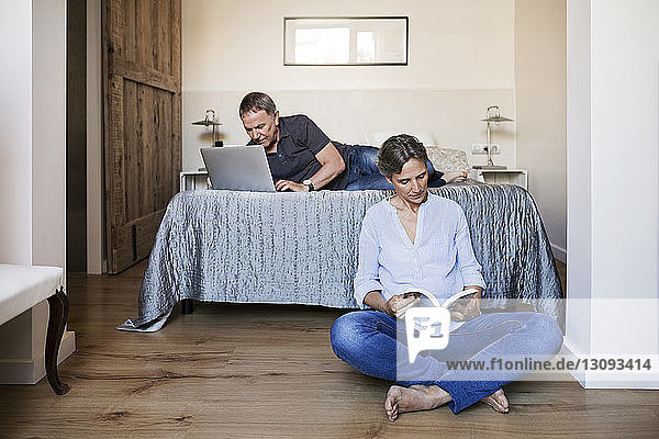 Senior couple using laptop and reading book in bedroom