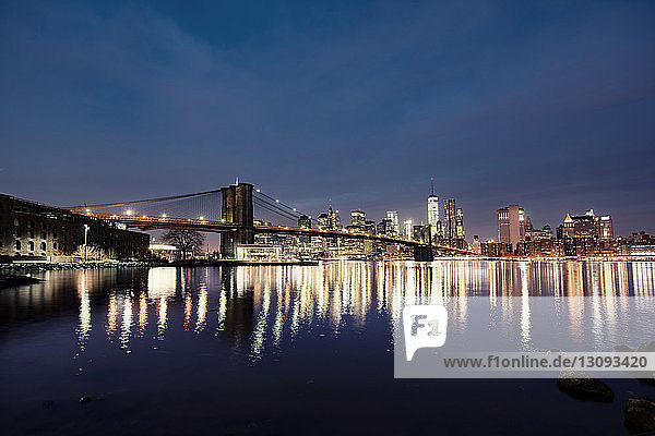Beleuchtete Brooklyn Bridge und Stadtlandschaft gegen den Himmel in der Dämmerung