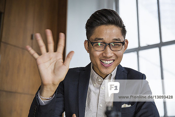 Happy businessman waving while sitting at office