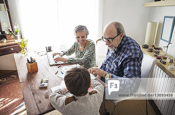 Glückliche Großeltern helfen dem Jungen zu Hause beim Zeichnen