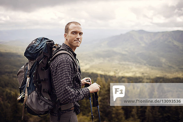 Porträt eines männlichen Wanderers  der einen Rucksack trägt  während er auf einem Berg steht