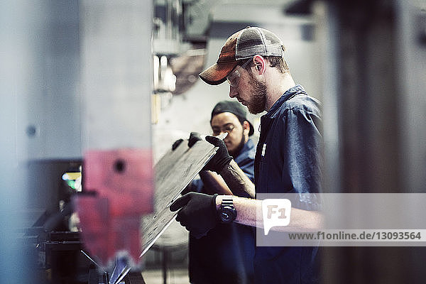 Young workers holding steel sheet by machinery in industry