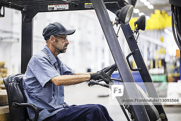 Side view of manual worker driving forklift while working in metal Steel Industry Factory