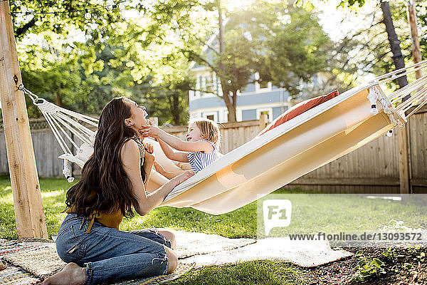Glückliche Mutter spielt mit Tochter in Hängematte sitzend im Hof