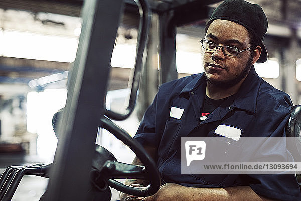 Worker looking away while sitting in forklift at industry