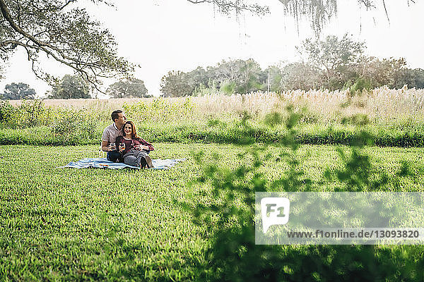 Couple holding drinks while relaxing at park