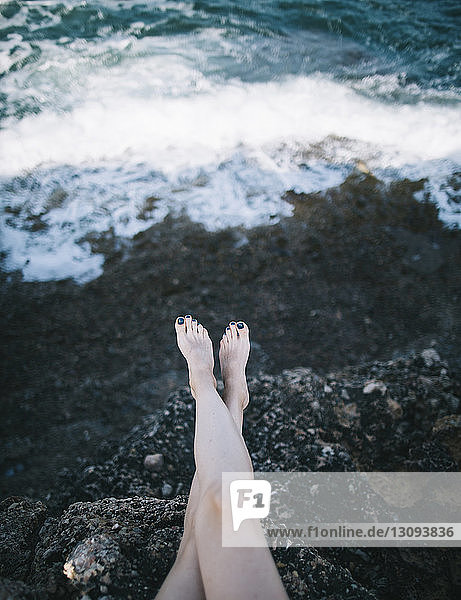 Niedriger Teil einer Frau  die auf einem Felsen am Meer sitzt