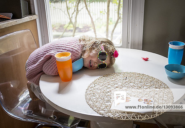 High angle view of baby girl wearing sunglasses lying on table at home