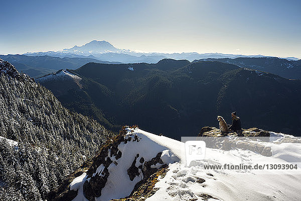 High angle view of man sitting with dog on mountain during winter