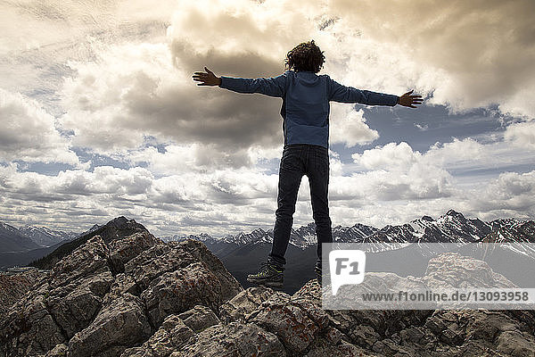 Rear view of man with arms outstretched standing on rocks against snowcapped mountains