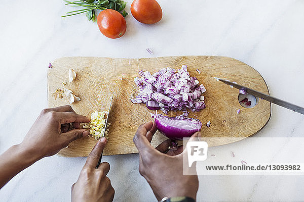 Cropped image of couple cutting onion and garlic on cutting board in kitchen