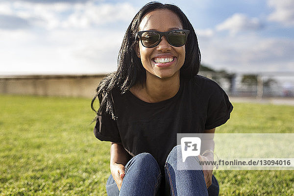 Porträt einer glücklichen Frau mit Sonnenbrille  die im Park sitzt