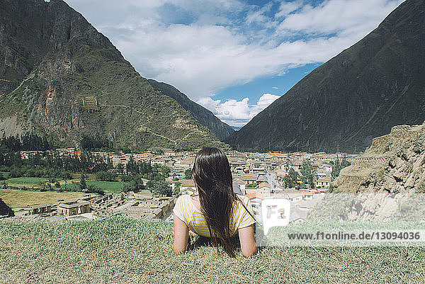 Rear view of female male hiker looking at village while sitting on mountain against sky at Pisac