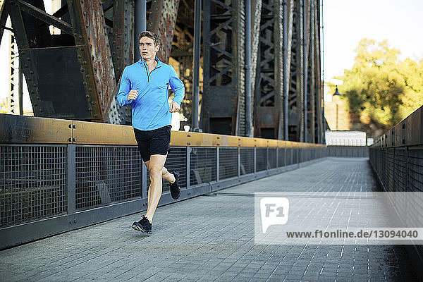 Full length of man running while exercising on bridge in city