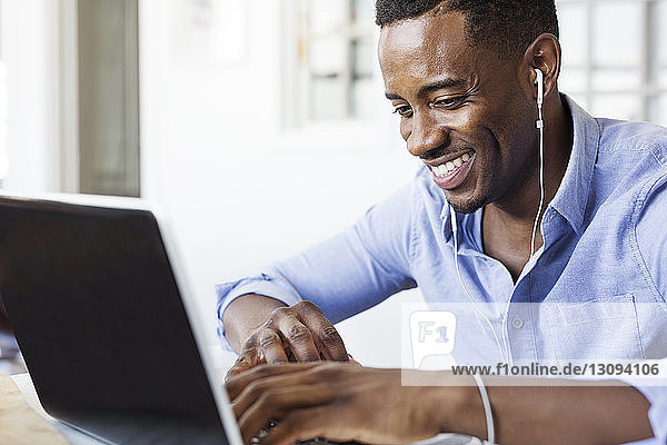 Glücklicher Mann hört Musik  während er zu Hause einen Laptop benutzt