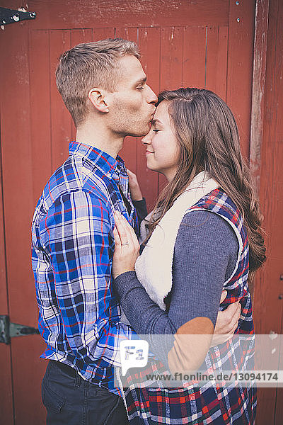 Ehemann küsst Frau bei geschlossener Tür auf die Stirn