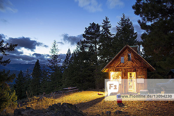 Beleuchtete Holzhütte im Wald bei Nacht