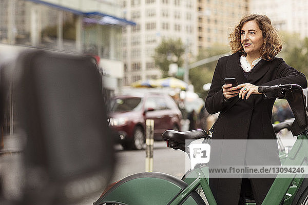 Woman using mobile phone while standing by bicycle rack in city