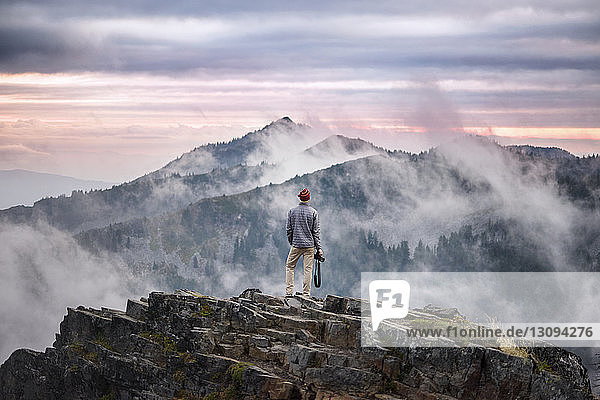 Rear view of photographer standing on cliff against cloudy sky