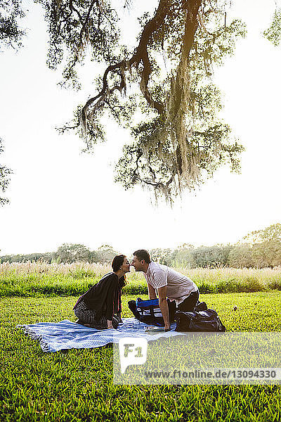Side view of couple looking at each other while kneeling on blanket against sky