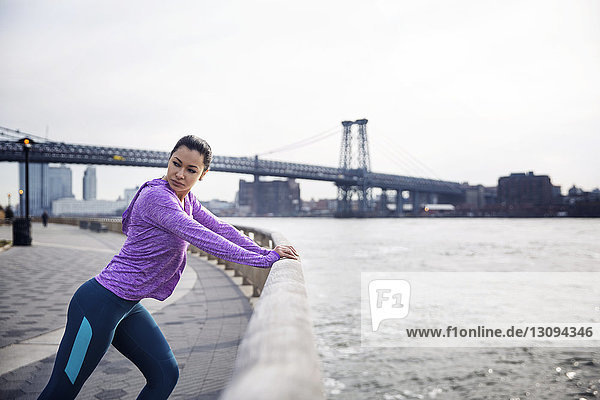 Seitenansicht einer entschlossenen Sportlerin  die sich auf einem Fußweg bewegt  mit der Williamsburg Bridge im Hintergrund