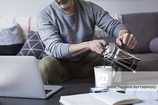 Ein Mann gießt zu Hause Kaffee aus der französischen Presse in eine Tasse