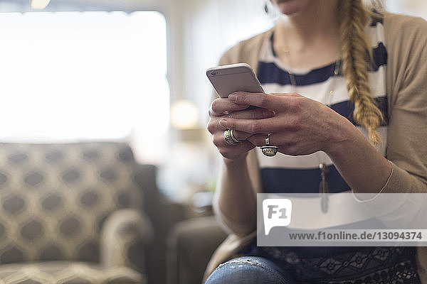 Midsection of female customer using smart phone while sitting in furniture store