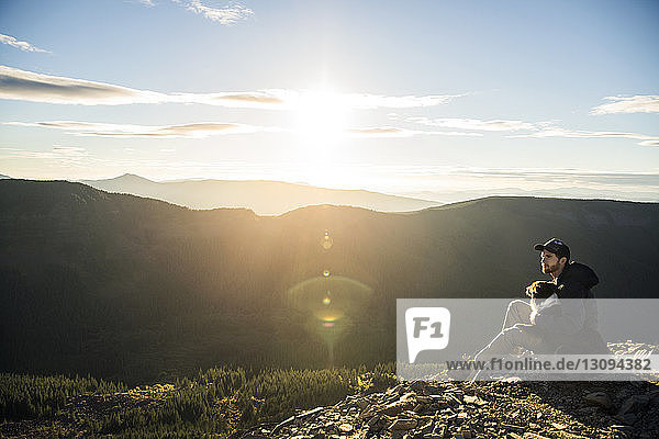 Man sitting with dog on cliff against mountain range