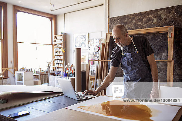 Male artist using laptop computer by painting in workshop
