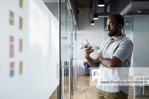 Junger Geschäftsmann benutzt Smartphone  während er im Bürokorridor steht