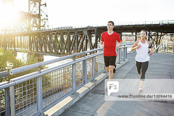 Friends jogging together on bridge against clear sky
