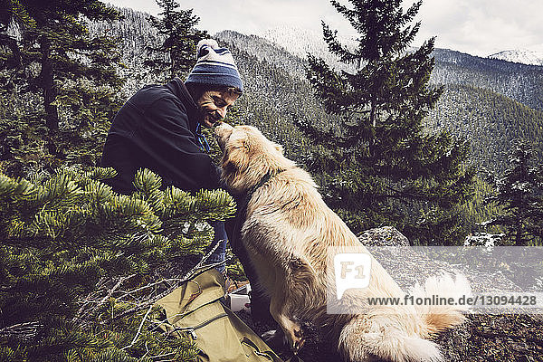Glücklicher männlicher Wanderer sieht Hund an  während er auf Berg sitzt
